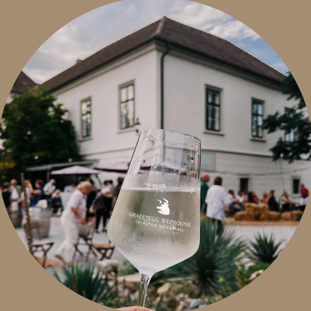 Weinglas mit Logo Grafenegg Weinlounge vor dem gut besuchten Gastgarten